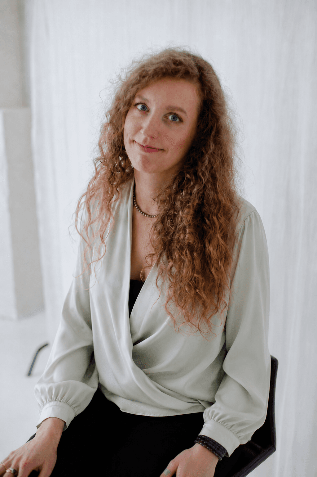Eglė seated in a sage silk blouse against a soft draped backdrop